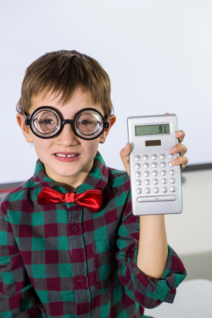 Portrait of boy holding calculator against whiteboard in classroomの写真素材