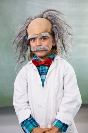 Portrait of boy dressed as scientist standing against board in classroomの写真素材