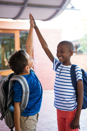 Playful classmates giving high-five at school corridorの写真素材