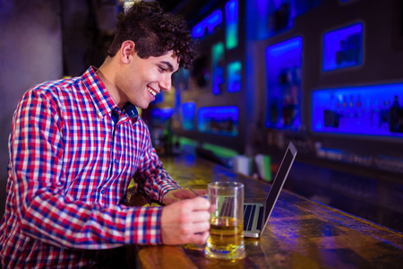 Smiling young man using laptop at counter in nightclubの写真素材
