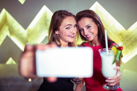 Beautiful happy women with cocktail taking selfie in nightclub