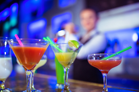 Cocktail glasses on counter with bartender standing in background at nightclubの写真素材
