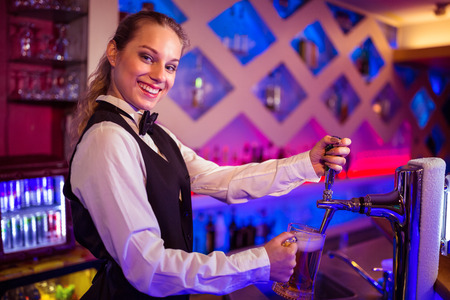 Portrait of happy barmaid pouring beer in glass at bar counter