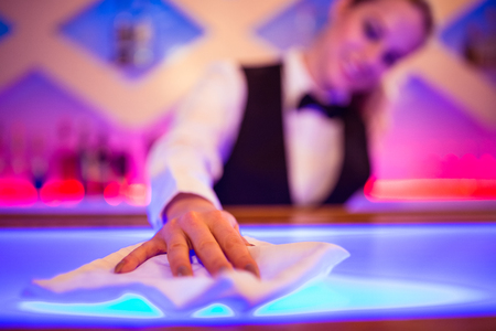 Barmaid cleaning illuminated bar counter with napkinの写真素材