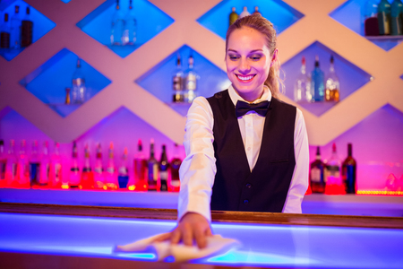 Barmaid smiling while cleaning illuminated bar counterの写真素材