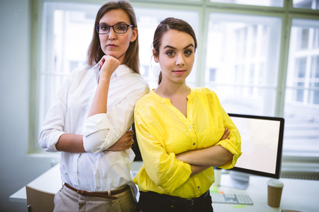 Portrait of confident young female colleagues standing with arms crossed at officeの写真素材