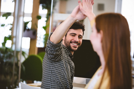Happy businessman giving high-five to female coworker in creative officeの写真素材
