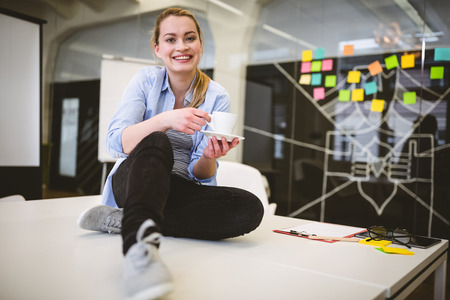Full length portrait of smiling businesswoman having coffee in meeting room