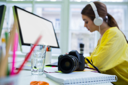 Close-up of camera on desk with young female executive working at officeの写真素材
