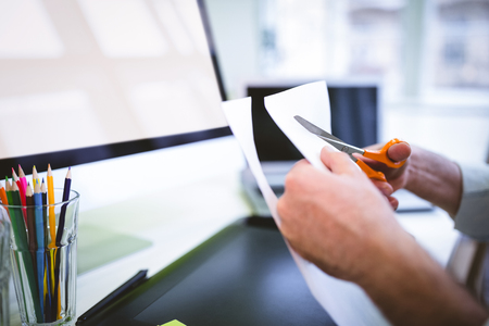 Cropped image of graphic designer cutting paper at desk in creative officeの写真素材