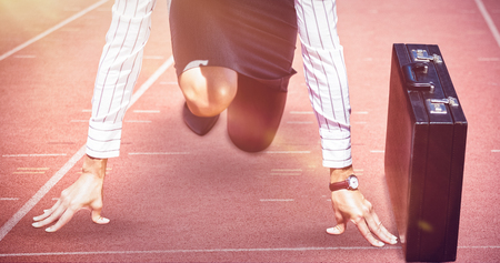 Businesswoman in starting position against focus of athletics track