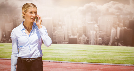 Smiling businesswoman on the phone against running track in front of cityの写真素材