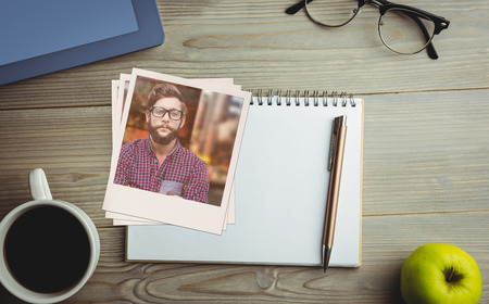 Happy hipster against wooden fence against overhead view of coffee with office suppliesの写真素材