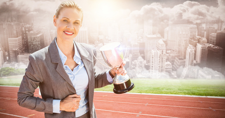 Successful businesswoman holding a trophy against composite image of track against cityの写真素材