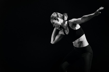 Front view of sportswoman is practising shot put  against black background