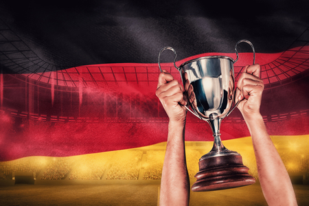 Portrait of smiling rugby player holding trophy against digitally generated german national flagの写真素材