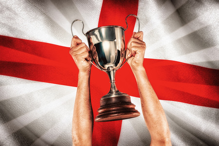 Portrait of smiling rugby player holding trophy against digitally generated english national flagの写真素材