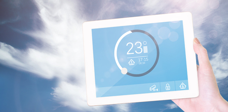 Feminine hand holding tablet against blue sky with clouds