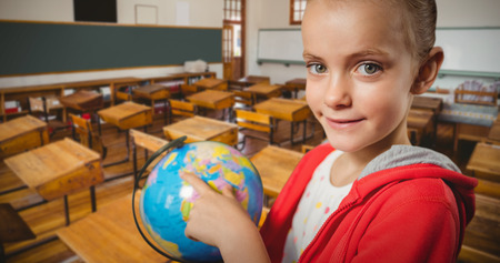 Cute girl pointing on globe against empty classroomの写真素材