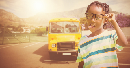 Young boy holding eyeglasses against yellow school bus waiting for pupils