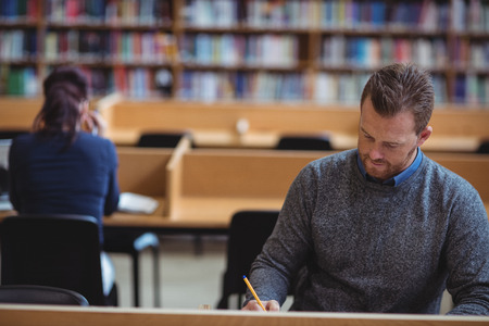 Mature student writing notes in college libraryの写真素材