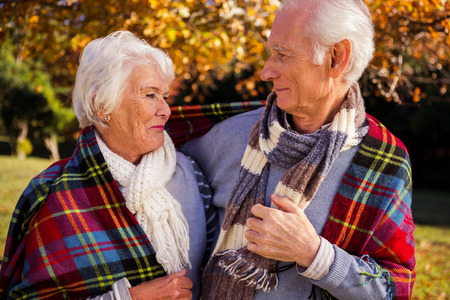 Senior couple embracing with a cover on their shoulder in a parkの写真素材