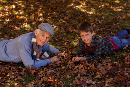 High angle portrait of grandfather and grandson lying on field at park during autumnの写真素材