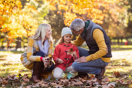 Happy family crouching against trees at park during autumn