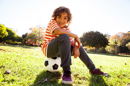 Portrait of smiling boy sitting on soccer ball at parkの写真素材