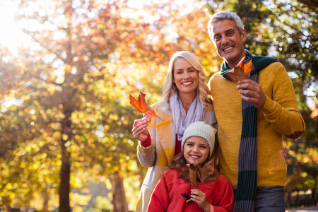 Portrait of happy family holding leaves against trees at park during autumn