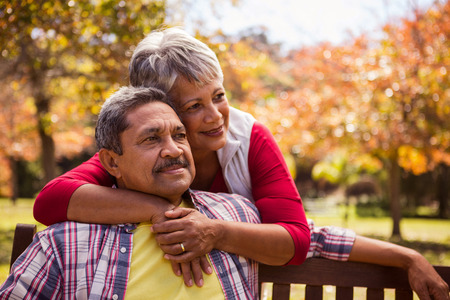 An elderly woman hugs her husband sitting on the bench in the parkの写真素材