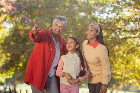 Happy grandmother pointing while standing with daughter and granddaughter at park
