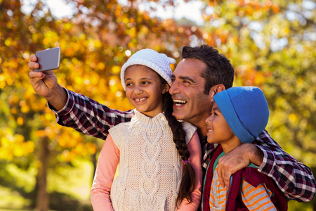 Happy father taking selfie with children against autumn trees at parkの写真素材