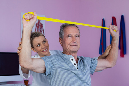 Senior man training with exercise band assisted by physiotherapist in clinicの写真素材