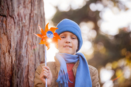 Low angle portrait of smiling boy holding pinwheel while standing at parkの写真素材