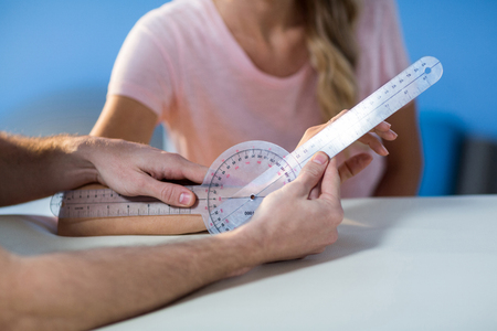 Physiotherapist examining female patients wrist with goniometer in the clinicの写真素材