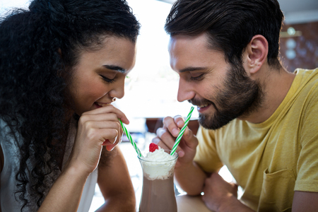 Smiling couple having milkshake in coffee shopの写真素材