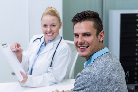 Smiling female doctor explaining prescription to patient on clipboard in clinicの写真素材