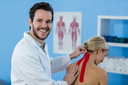 Physiotherapist sticking tape on female patient in clinicの写真素材