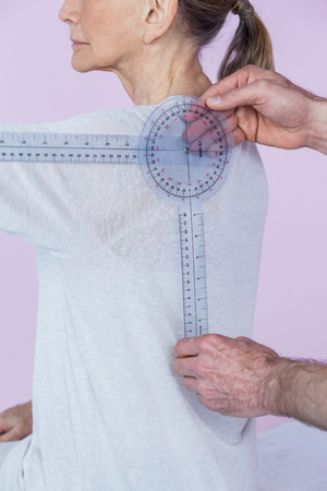 Physiotherapist measuring female patients back with medical ruler in clinic