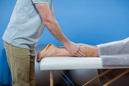 Male physiotherapist giving knee massage to female patient in clinicの写真素材