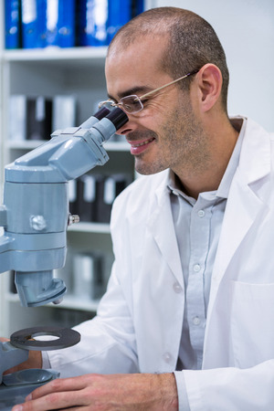 Smiling male optometrist looking through microscope in ophthalmology clinicの写真素材
