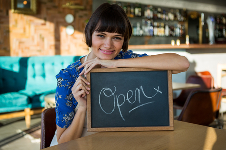 Portrait of smiling woman sitting in the coffee shop with a open signの写真素材