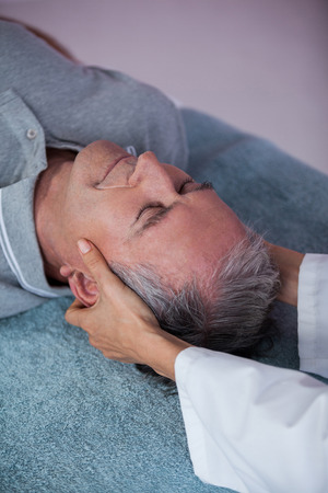 Senior man receiving neck massage from physiotherapist in clinicの写真素材