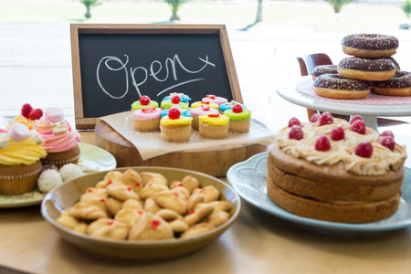 Close-up of various sweet foods on table with open signboard in cafeteriaの写真素材