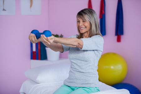Smiling senior woman holding dumbbell in clinicの写真素材