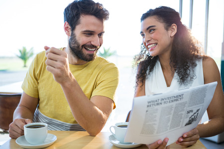 Smiling couple reading newspaper while having coffee in coffee shopの写真素材