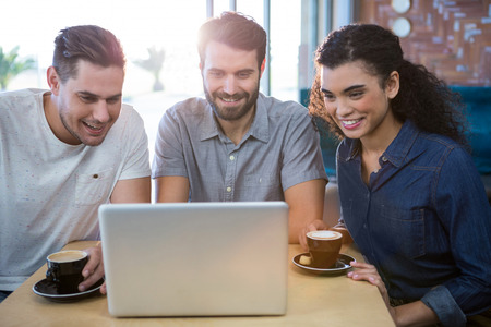 Smiling friends using a laptop in the coffee shopの写真素材