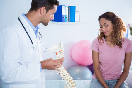 Physiotherapist explaining spine model to patient in clinicの写真素材