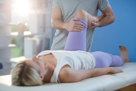 Male physiotherapist giving knee massage to female patient in clinicの写真素材